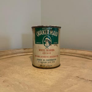 May include: A vintage metal can of Quaker Maid Premium Wheel Bearing Grease. The can is green and white with a red and white illustration of a woman. The text on the can reads "Premium Quaker Maid", "Wheel Bearing Grease", "For Farm, Automotive, Industrial Uses", "Quaker Oil Corporation", "St. Louis, Mo. 63147 U.S.A.", and "Net Wt. 1 Pound".