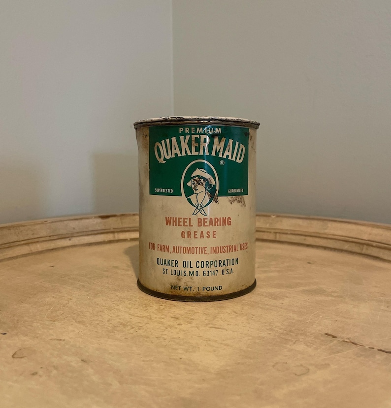 May include: A vintage metal can of Quaker Maid Premium Wheel Bearing Grease. The can is green and white with a red and white illustration of a woman. The text on the can reads "Premium Quaker Maid", "Wheel Bearing Grease", "For Farm, Automotive, Industrial Uses", "Quaker Oil Corporation", "St. Louis, Mo. 63147 U.S.A.", and "Net Wt. 1 Pound".