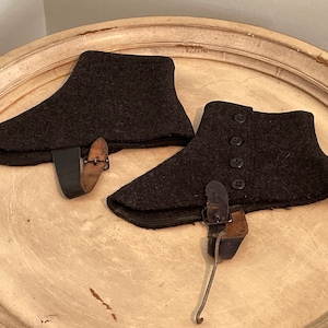 May include: Two pairs of dark gray wool boot gaiters with leather straps and buckles. One pair has four black buttons.