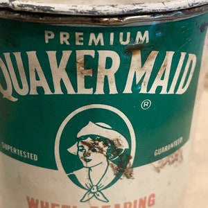 May include: A vintage tin can of Quaker Maid Premium Wheel Bearing Grease. The can is green and white with a red and white logo of a woman wearing a white hat and a green and white sailor collar. The text "SUPER TESTED" and "GUARANTEED" are printed on the can.