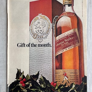 May include: A vintage advertisement for Johnnie Walker Red Label Scotch whisky. The ad features a bottle of the whisky, a red box, and a festive holly sprig. The text reads "Gift of the month." "Imported by Dry Corporation New York, NY." "Blended Scotch Whisky." "Johnnie Walker Red Label." "4/5 Quart." "Blended and Bottled in Scotland." "86 Proof." "Chest 1880, 1883, 1885, 1887." "Awards Dunedin 1890, Jamaica 1891, Kimberley 1892, Brisbane 1897." "Johnnie Walker Red, world's best selling Scotch (Because it's so smooth)"