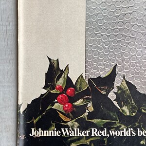 May include: A vintage advertisement for Johnnie Walker Red, the world's best-selling Scotch whisky. The ad features a festive holly sprig with red berries and the text "Gift of the month".