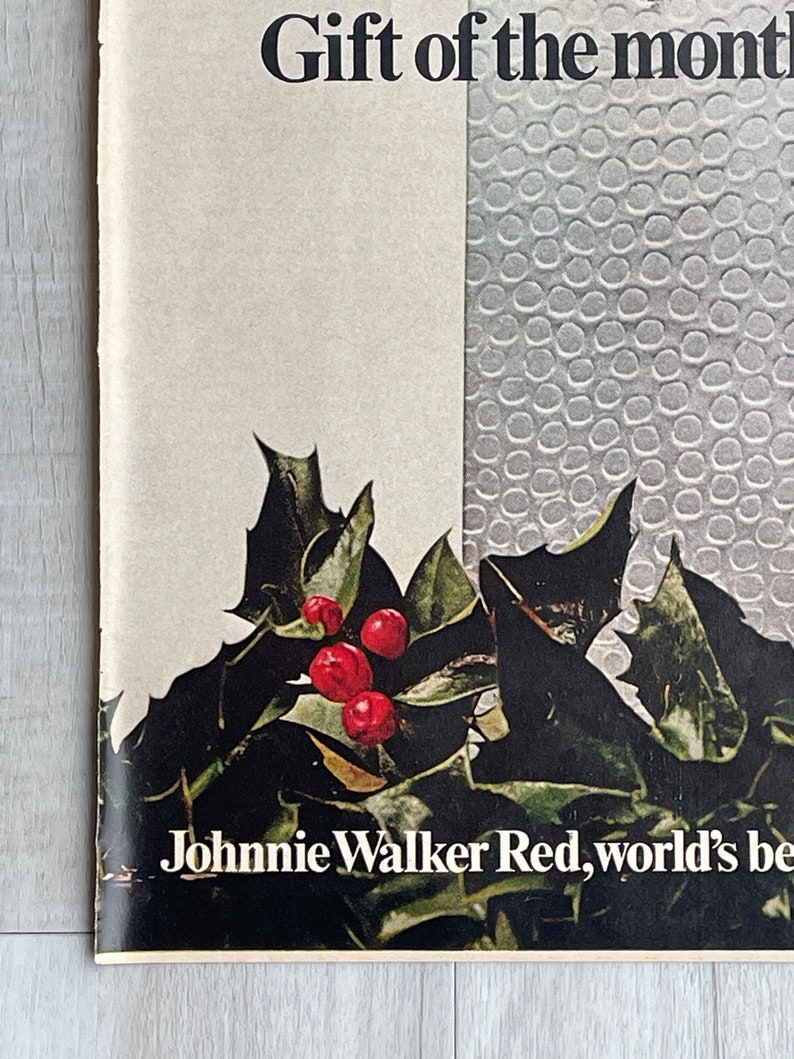 May include: A vintage advertisement for Johnnie Walker Red, the world's best-selling Scotch whisky. The ad features a festive holly sprig with red berries and the text "Gift of the month".