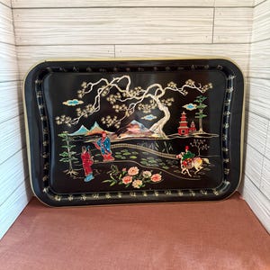 May include: A rectangular black serving tray with a gold rim and a decorative Asian-inspired scene. The scene features figures, trees, mountains, and a pagoda. The tray is approximately 18 inches long and 12 inches wide.