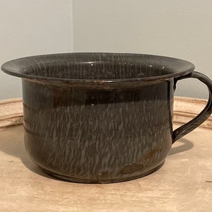 May include: A grey enamel chamber pot with a single handle. The pot has a mottled, wood-grain pattern.