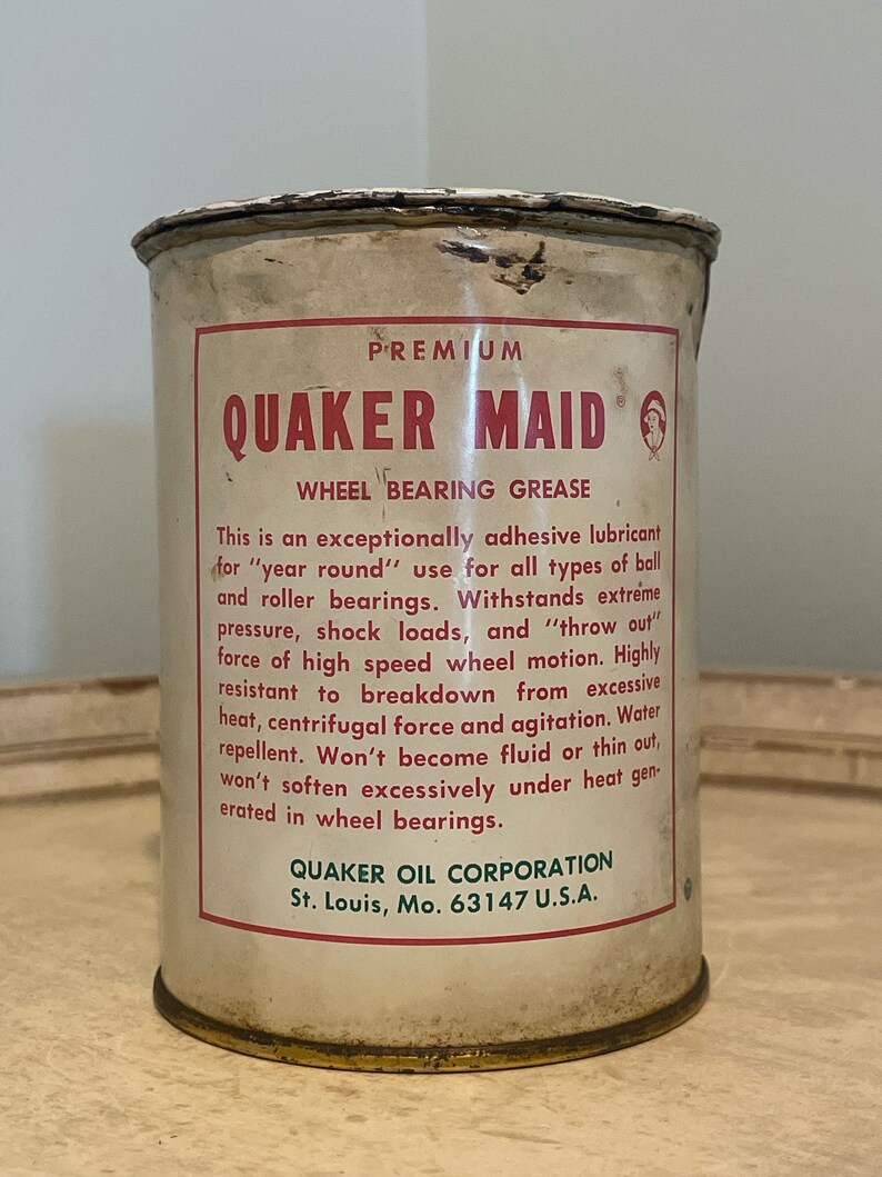 May include: A white metal can with a red and white label. The label reads "PREMIUM QUAKER MAID WHEEL BEARING GREASE". The text on the label describes the product as an exceptionally adhesive lubricant for "year round" use for all types of ball and roller bearings. The label also states that the product is water repellent and won't become fluid or thin out under heat generated in wheel bearings. The label also includes the company name and address: "QUAKER OIL CORPORATION St. Louis, Mo. 63147 U.S.A."