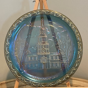 May include: A blue iridescent glass plate with a raised image of Independence Hall in Philadelphia. The plate has a scalloped edge and the words "Independence Hall" are printed on the bottom.