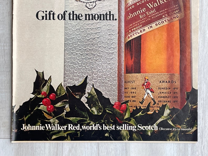 May include: A bottle of Johnnie Walker Red Label Scotch whisky with a red and gold label. The bottle is surrounded by holly and berries. The text on the label reads "Johnnie Walker Red Label, world's best selling Scotch (Because it's so smooth)".