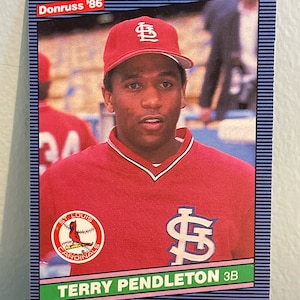 May include: A baseball card featuring Terry Pendleton of the St. Louis Cardinals. The card has a blue border with the text "Donruss '86" at the top. Pendleton is wearing a red Cardinals uniform and cap. The team logo is visible.