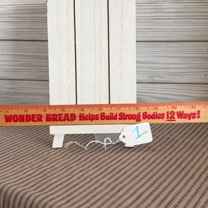 May include: A wooden ruler with red text reading "WONDER BREAD Helps Build Strong Bodies 12 Ways!" is displayed in front of a white wooden easel. A small white tag with the number "1" is attached to the ruler.