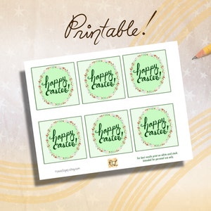 May include: Printable sheet of six square gift tags with a green background and a floral wreath with the text "Happy Easter!" in black cursive.