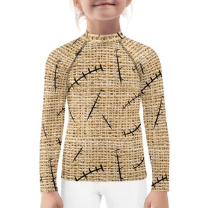 May include: A long-sleeved shirt for kids with a brown burlap pattern and black stitching. The shirt has a mock neck and long sleeves.