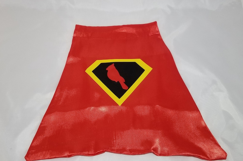 May include: Red satin cape with a yellow and black diamond-shaped emblem featuring a red cardinal silhouette.