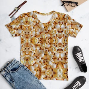 May include: A white and yellow popcorn-patterned t-shirt with a scoop neck. The shirt is surrounded by a pair of black sneakers, blue jeans, a watch, and a notebook with glasses.