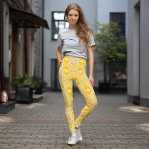 May include: Yellow leggings with a repeating white and yellow pattern. The leggings are high-waisted and form-fitting. The model is wearing a gray t-shirt and white sneakers. The leggings are made of a soft, stretchy material.