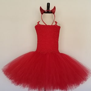May include: Red tulle tutu with a red crochet bodice and a red devil horn headband.  The tutu is on a mannequin.  Super Capes and More.