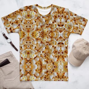 May include: A short-sleeved t-shirt with a popcorn pattern. The shirt is white, yellow, and brown. A brown leather watch, tan cap, and tan pants are also visible.