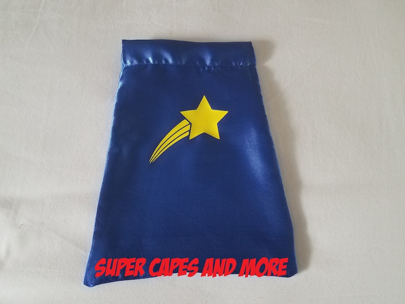 May include: Blue satin cape with a yellow star and a shooting star design. The cape has the text "SUPER CAPES AND MORE" printed on the bottom.