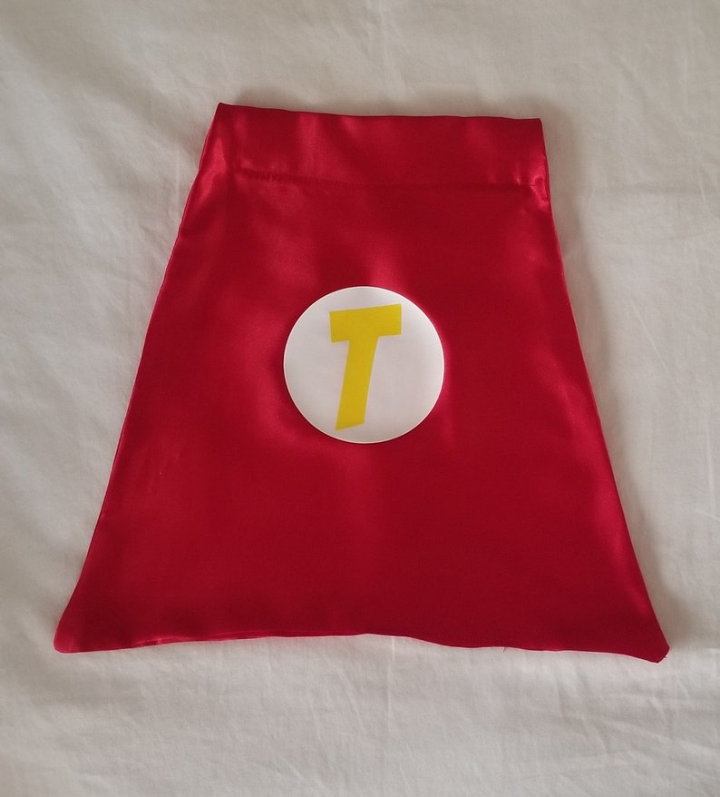 May include: Red satin cape with a white circle and a yellow letter T in the center.