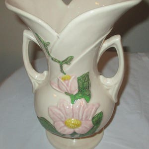 Peut inclure: Un vase en c&eacute;ramique vintage &agrave; deux anses, avec un motif floral de fleurs roses et jaunes avec des feuilles vertes sur un fond cr&egrave;me.