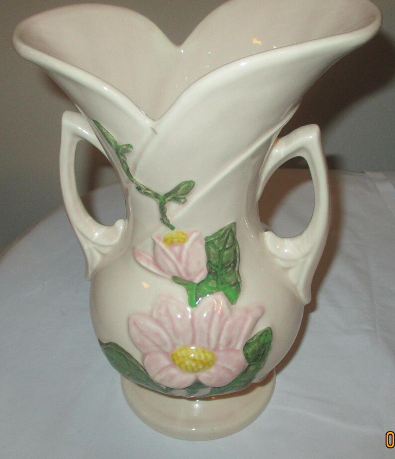 Peut inclure: Un vase en c&eacute;ramique vintage &agrave; deux anses, avec un motif floral de fleurs roses et jaunes avec des feuilles vertes sur un fond cr&egrave;me.