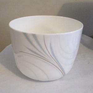 May include: A white ceramic bowl with a rounded shape. The bowl features a decorative pattern of blue and brown curved lines. The interior of the bowl is a lighter shade of white.