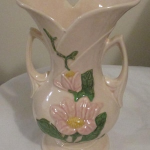 Peut inclure: Un vase en c&eacute;ramique rose vintage avec deux anses et un motif floral. Le vase pr&eacute;sente des fleurs roses avec des feuilles vertes.