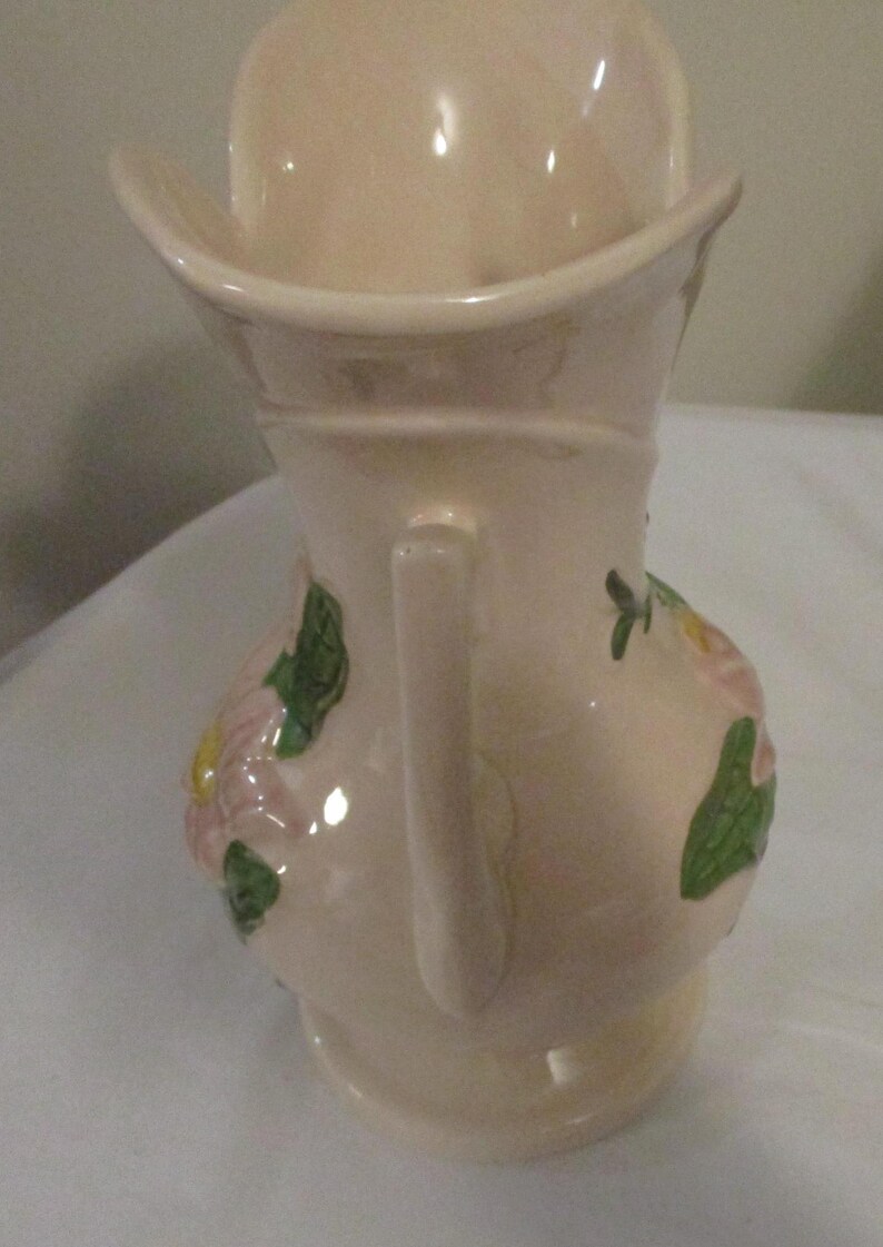 Peut inclure: Un pichet en c&eacute;ramique rose avec un motif floral. Le pichet a une anse et une large ouverture. Les fleurs sont roses, jaunes et vertes.