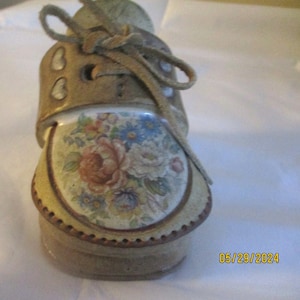May include: A ceramic shoe shaped like a boot with a floral design and a brown leather lace. The shoe is decorated with a floral pattern and has a brown leather lace.