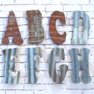 May include: Rustic metal letters spelling out the word "ABCDEFGH" in a distressed, galvanized finish. The letters are arranged in two rows on a white brick wall.