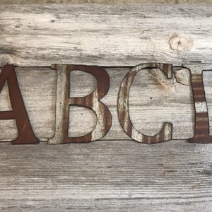 May include: Metal letters spelling out "ABCD" in a rustic style. The letters are painted in a brown and white striped pattern, giving them a vintage look.