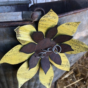 K&ouml;nnte beinhalten: Eine gelbe und braune Metallsonnenblume mit Drahtverzierungen, die an einem verzinkten Metalleimer befestigt ist.