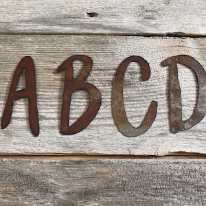 May include: Four rusty metal letters spelling out "ABCD" on a weathered wooden background.