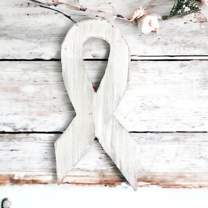 May include: A white wooden ribbon tied in a bow, against a whitewashed wood background.