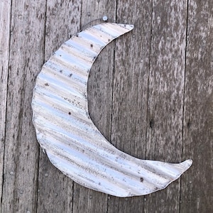 May include: A white metal crescent moon wall decor with a distressed finish. The moon is made of corrugated metal and has a rustic look.