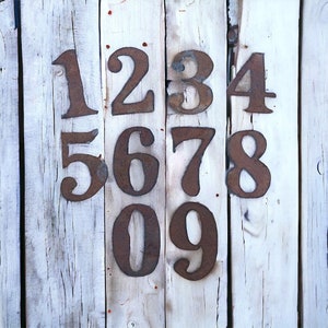 May include: A weathered wooden surface with the numbers 1 through 9 painted in rusty brown metal. The numbers are arranged in three rows, with the first row being 1, 2, 3, and 4, the second row being 5, 6, 7, and 8, and the third row being 9.