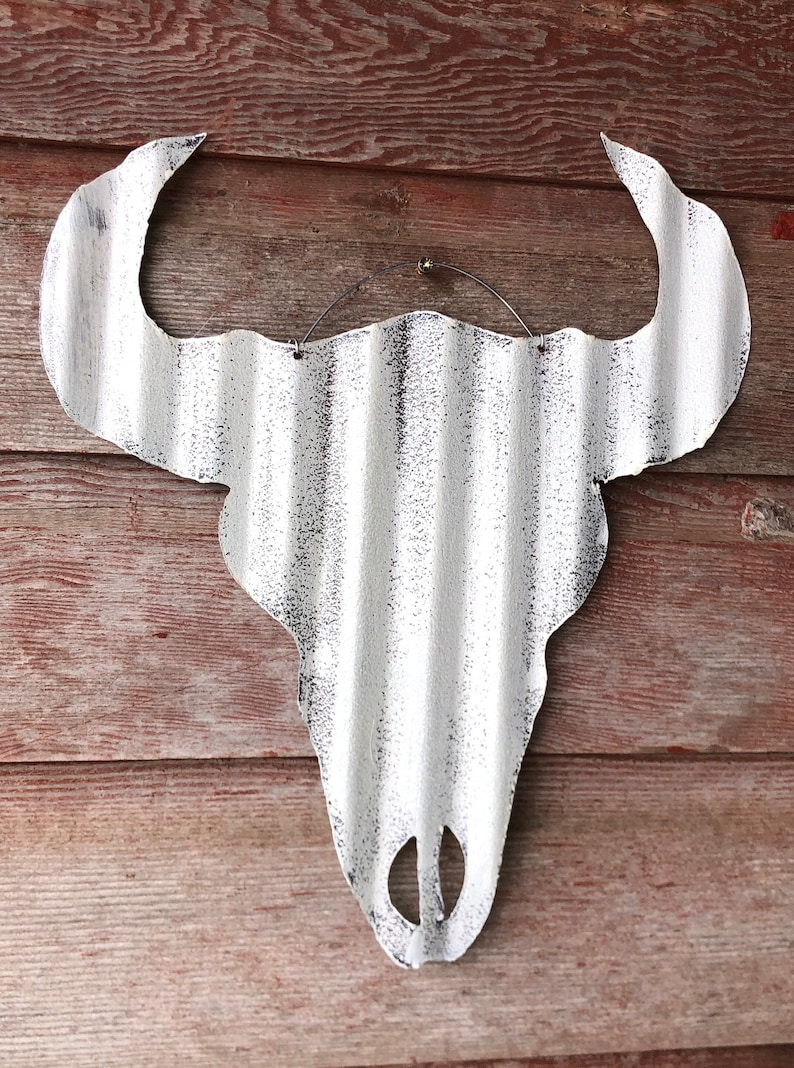 Op de afbeelding: Witte metalen stieren schedel wanddecoratie met een verweerde afwerking. De schedel is gemaakt van gegolfd metaal en heeft een rustieke uitstraling.