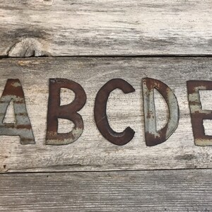 May include: Rustic metal letters spelling out the word "ABCDE" on a wooden background. The letters are a light gray color with rust accents.