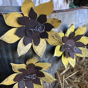 K&ouml;nnte beinhalten: Drei gelbe Metall-Sonnenblumen mit braunen Zentren und Draht-Akzenten. Die Sonnenblumen sind in einem verzinkten Metalleimer angeordnet.