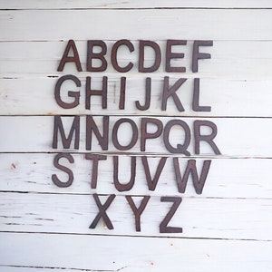 May include: A set of rusty metal letters spelling out the alphabet, A through Z, arranged in rows on a white wooden background.