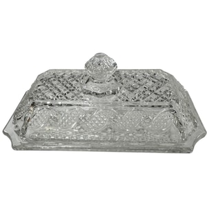 May include: A clear, rectangular glass butter dish with a diamond-cut pattern. The dish has a lid with a knob on top. The edges of the dish are slightly scalloped. The butter dish is designed to hold butter.