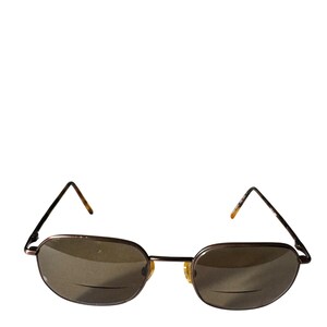 May include: A pair of reading glasses with a bronze-colored metal frame and oval lenses. The temples have a tortoiseshell pattern. The lenses are tinted and have a line at the bottom, indicating the reading portion of the lens.