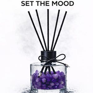 May include: A clear glass aromatherapy diffuser with black reeds and a black cap, tied with a black bow. The bottle is filled with purple stones. The text "SET THE MOOD" is at the top.