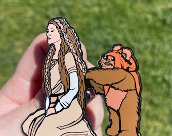 Può includere: Uno spillo in smalto che rappresenta una versione cartoon della Principessa Leia di Star Wars con un Wookiee che tira i suoi capelli. Lo spillo è di colore marrone e arancione.