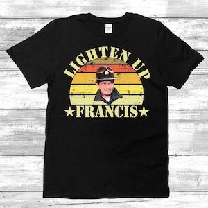 May include: Black t-shirt with a vintage-style graphic of a man in a military hat. The graphic says "Lighten Up Francis" with a star on either side of the name.