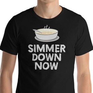 May include: Black t-shirt with a white graphic of a bowl of soup with a spoon and the text "SIMMER DOWN NOW".
