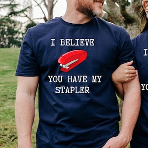 Könnte beinhalten: Ein Paar trägt passende marineblaue T-Shirts mit einer roten Heftergrafik und dem Text "Ich glaube, du hast meinen Hefter".
