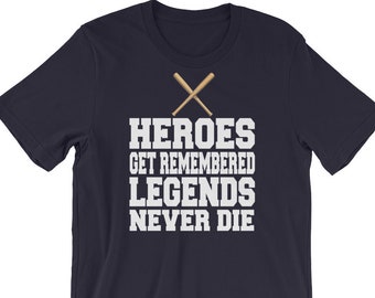 May include: Navy blue t-shirt with the text "HEROES GET REMEMBERED LEGENDS NEVER DIE" in white block letters. Two crossed baseball bats are above the text. The shirt is a short-sleeved crew neck.