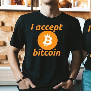 May include: Two people wearing black t-shirts with the text "I accept bitcoin" and a bitcoin symbol printed on the front.