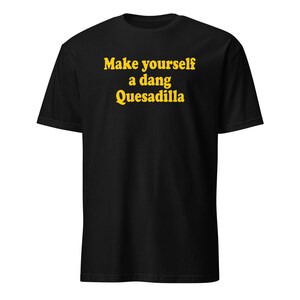 Puede incluir: Camiseta negra con el texto amarillo "Make yourself a dang Quesadilla", un diseño juguetón y humorístico. La camiseta es de estilo cuello redondo, adecuada para uso casual.